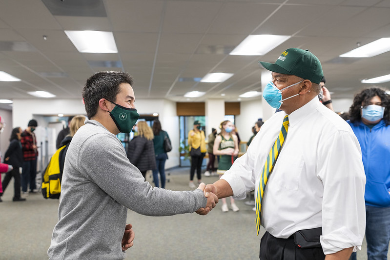 A student shakes hands with a man in a tie at a networking event.