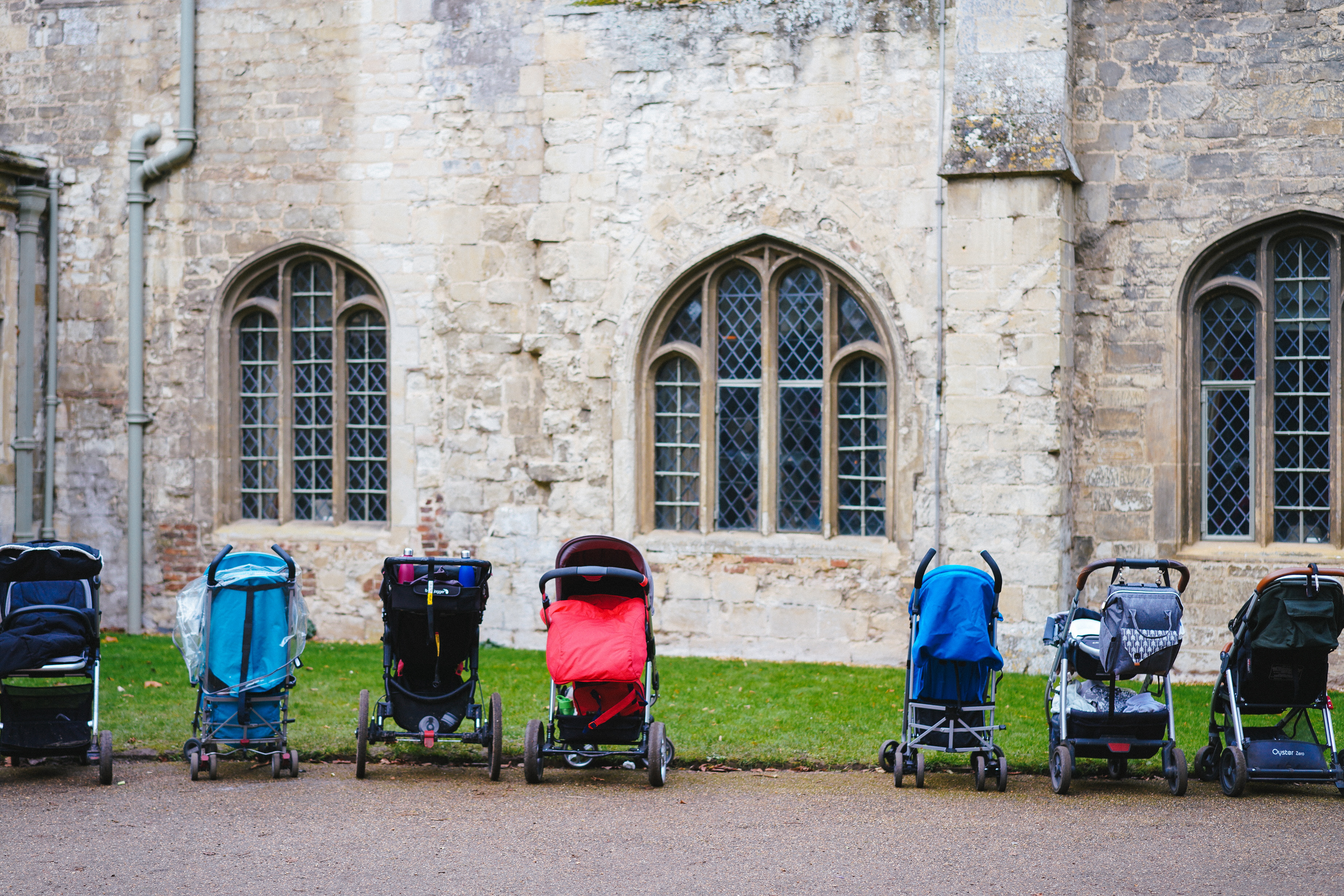 A line of infant's strollers, unattended, beside an empty building.