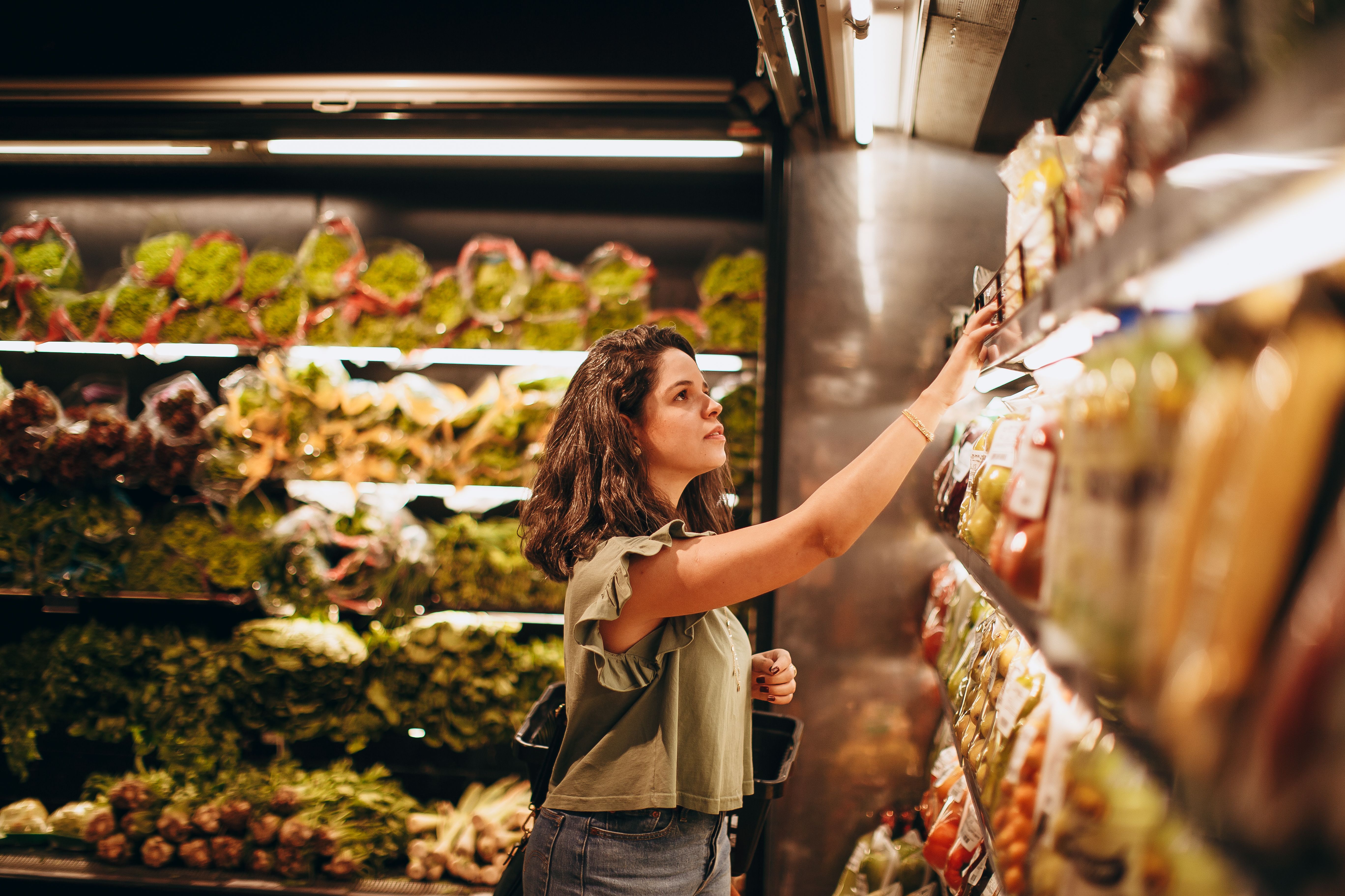 A woman shopping in a grocery store reaches for produce